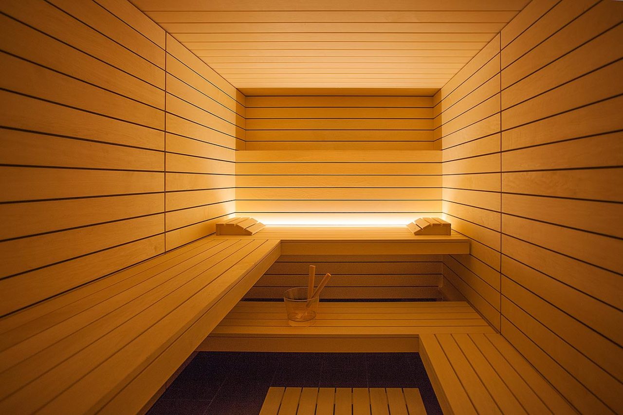 Moderne Design Sauna mit Hinterwandofen im geradlinigen modernen Stil. Helle Espe als scharfkantiges Profilholz mit Schattenfuge. Indirekte LED Beleuchtung. Moderne Heimsauna.