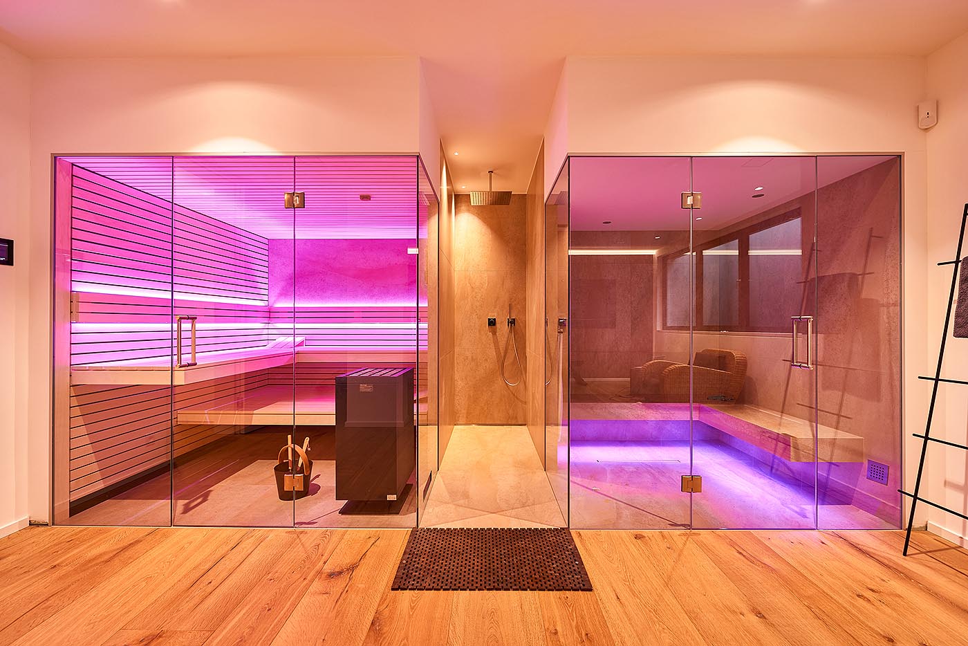 Kombination aus geradliniger Sauna mit Glasfront und Dampfbad mit Glasfront im Privat SPA. Symmetrische Anordnung mit mittiger Dusche. Schwebende Bänke mit indirekter LED Beleuchtung.
