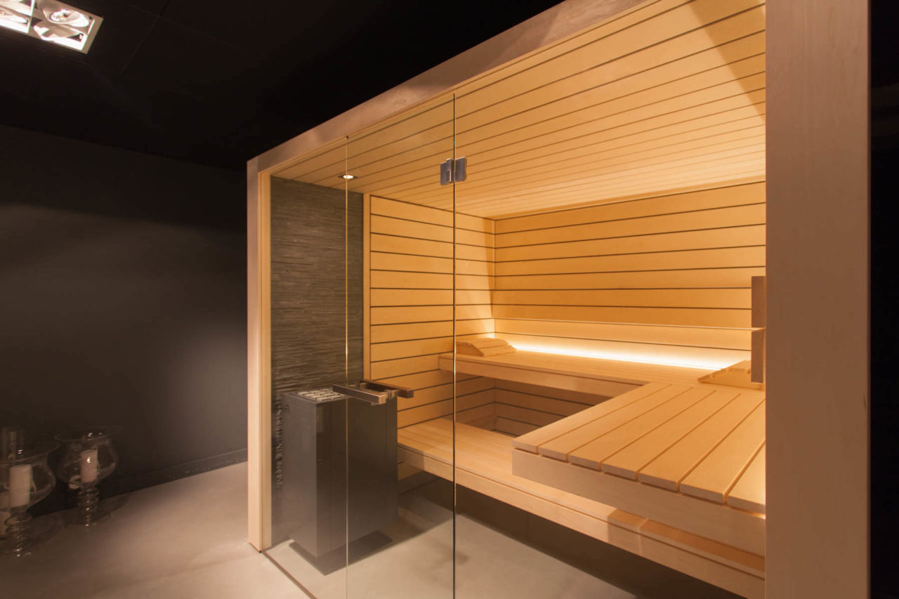 Sauna design lumineux avec façade en verre et mur en pierre naturelle derrière le poêle de sauna
