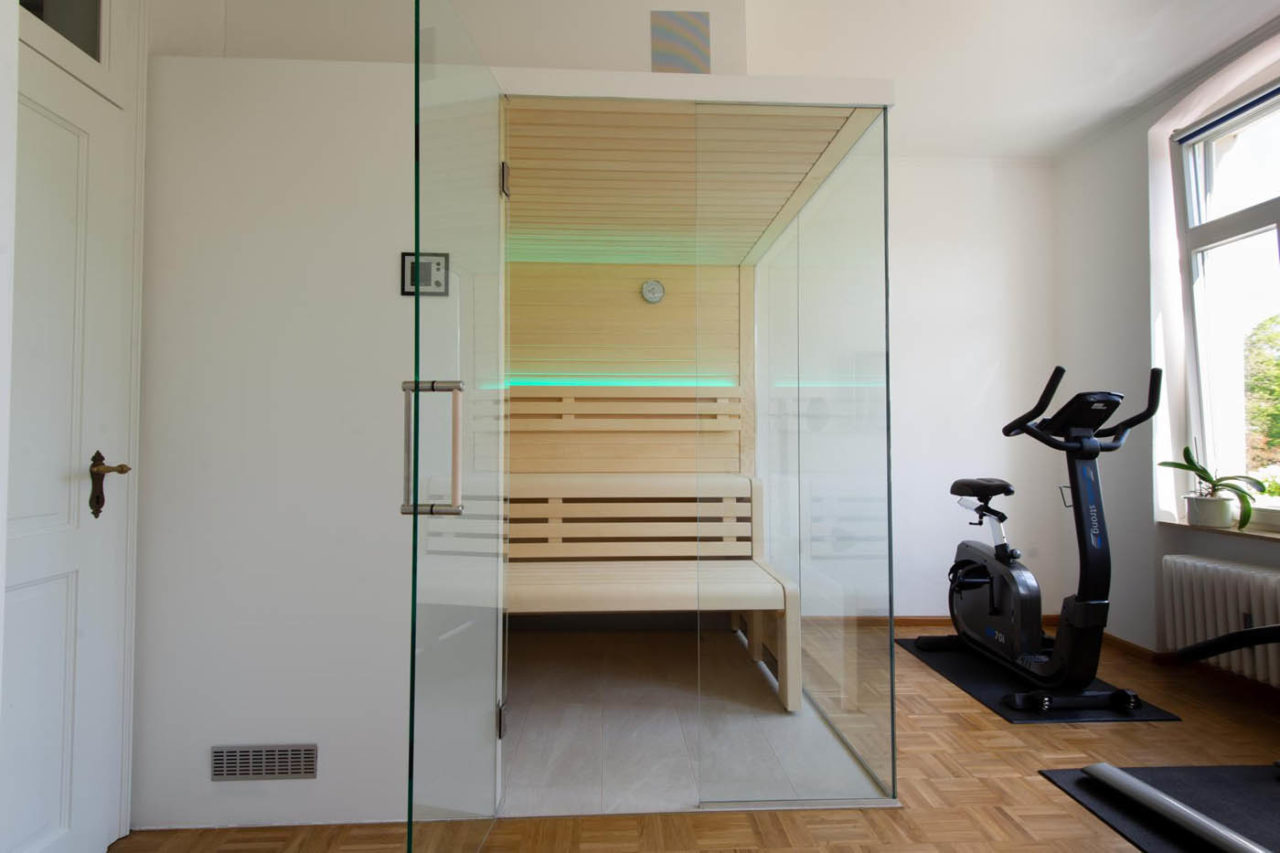 Moderne Sauna Zuhause mit Glasecke in hellem Saunaholz und schicker Beleuchtung. Lösung als Ecksauna.