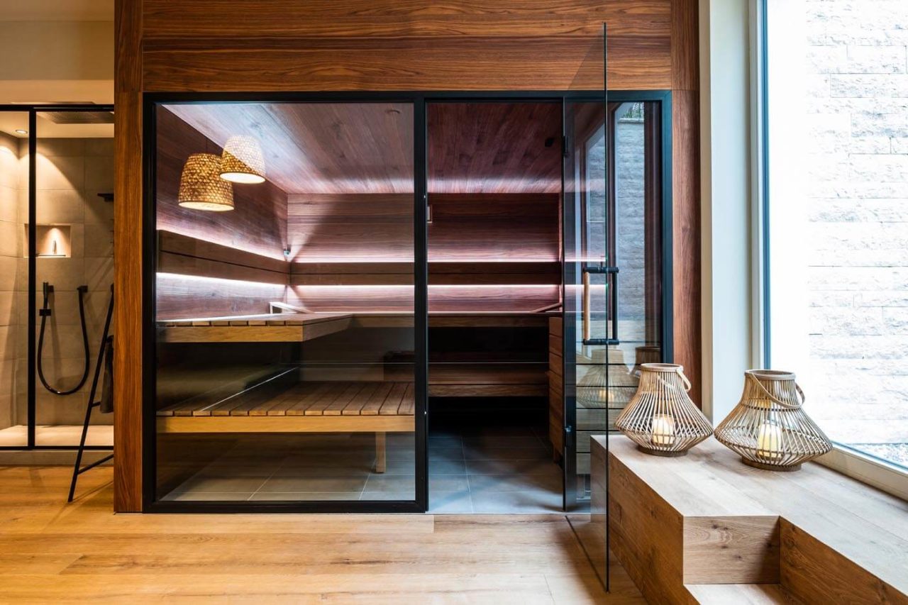 Design Sauna mit Glasfront in Nussbaumholz in einem privaten Wellnessbereich. Indirekte Beleuchtung hinter den Rückenlehnen. Schwebende Saunabänke.