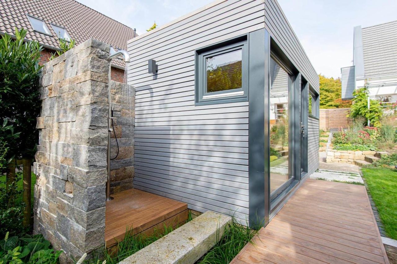 Modern made-to-measure garden sauna in the garden with partial glazing and relaxation room. Exterior cladding in rhombus profiled wood. Design garden sauna.