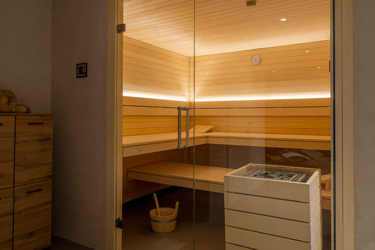 Helle Design Sauna mit indirekter LED Beleuchtung und großzügiger Glasecke. Voll integrierte Einbausauna nach Maß.