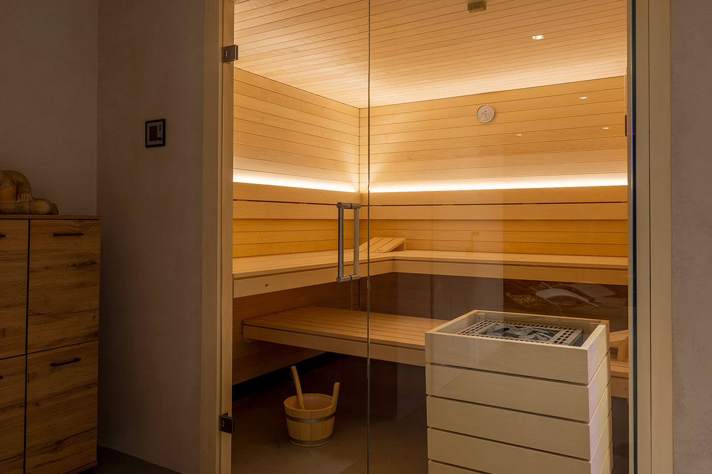 Helle Design Sauna mit indirekter LED Beleuchtung und großzügiger Glasecke. Voll integrierte Einbausauna nach Maß.