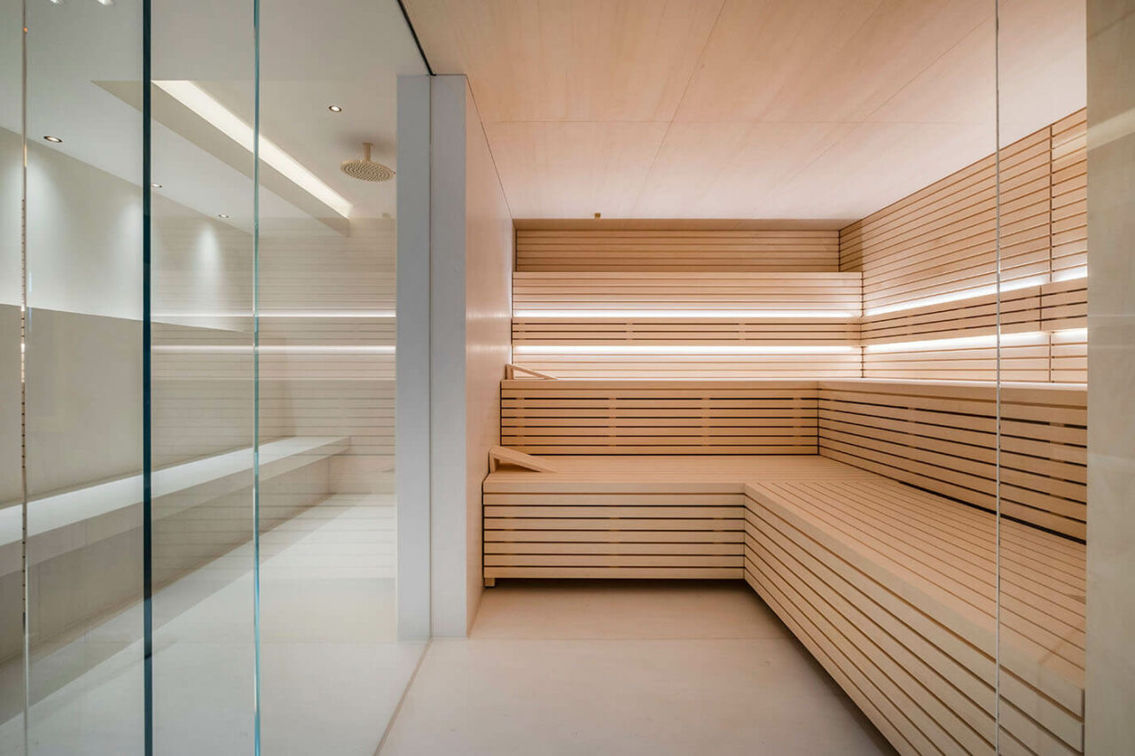 Design Sauna im Bauhausstil mit Hinterwandofen. Saunaholz: helle Espe in Stäbchenoptik. Große Glasfront, LED Beleuchtung, Hinterwandofen.