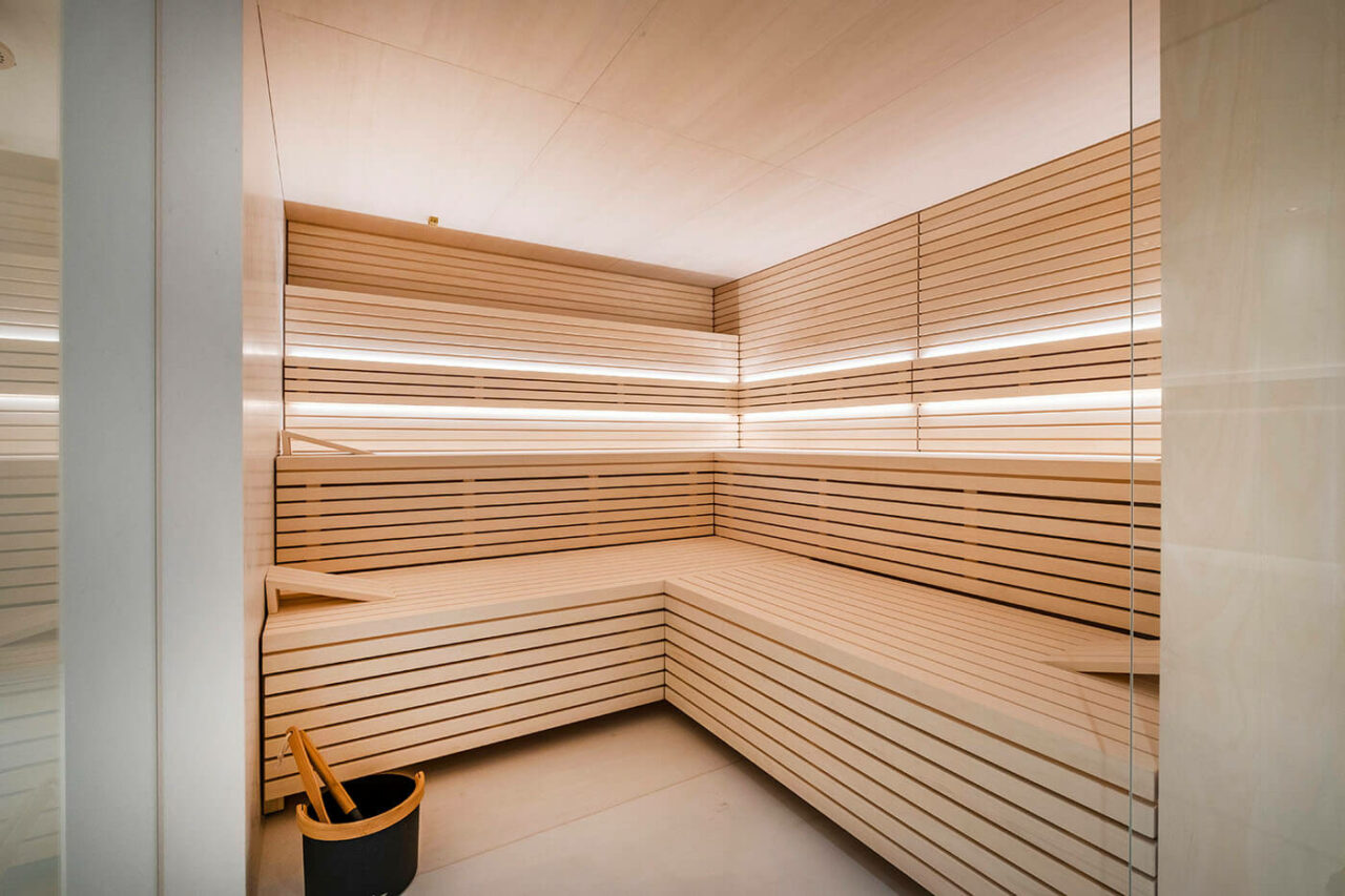 Design Sauna im Bauhausstil mit Hinterwandofen. Saunaholz: helle Espe in Stäbchenoptik. Große Glasfront, LED Beleuchtung, Hinterwandofen.