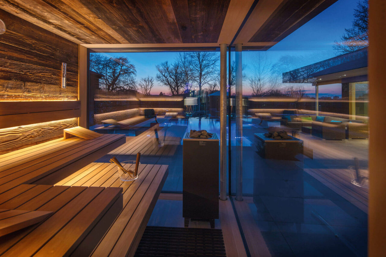 Saunabau nach Maß. Große Sauna Ausstellung: Design Sauna direkt vom Saunahersteller. Außensauna bzw. Gartensauna mit Glasfront in Altholz und Saunabänke in Thermo-Espe mit frei stehendem Saunaofen.