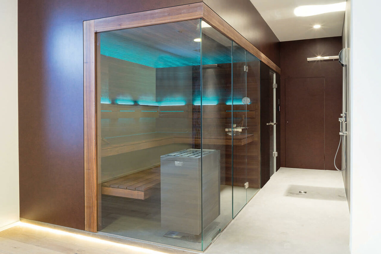 Saunabau Köln: massgefertigte Designsauna in Nussbaum mit Glasecke und frei stehendem Saunaofen