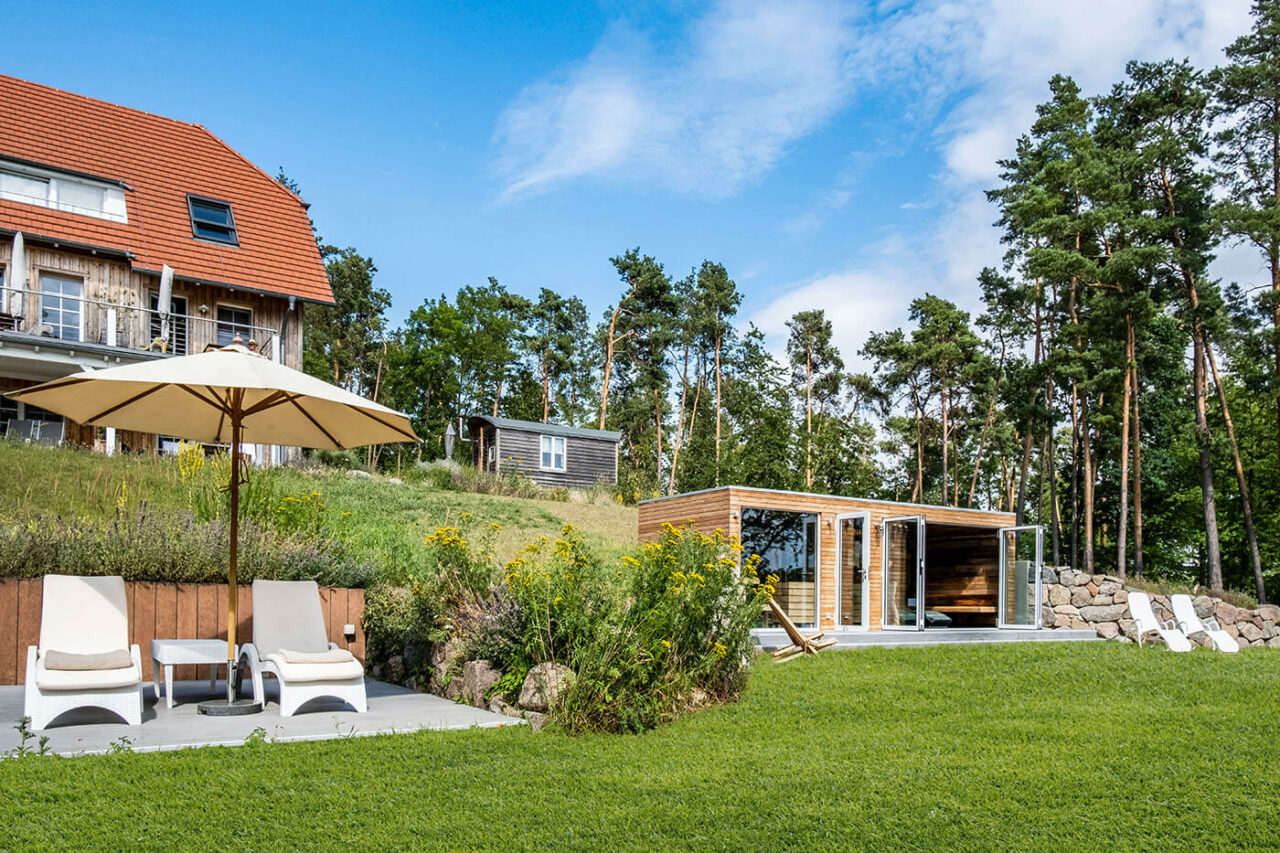 Außensauna Hotel: Gartensauna im Außenbereich direkt am See beim Hotel Lichtenberg mit Ruheraum und Dusche. Innengestaltung in Altholz, Außengestaltung passend zum Hotel.