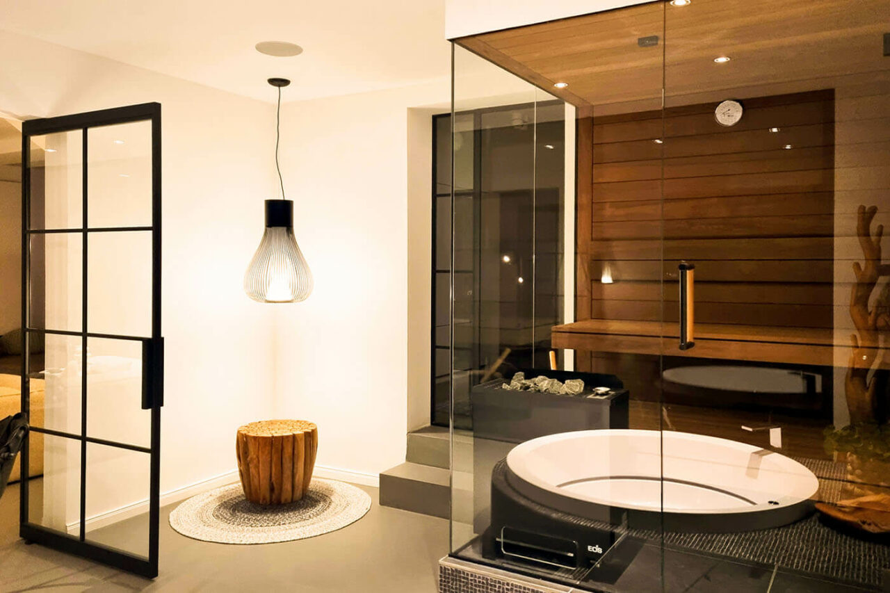 Design Ecksauna in Thermo Espenholz mit zweiseitige Verglasung und schwebenden Saunabänken. Modernes Bad in schwarz-weißer Gestaltung mit eingelassener Badewanne. Sauna nach Maß aus der corso sauna manufaktur.