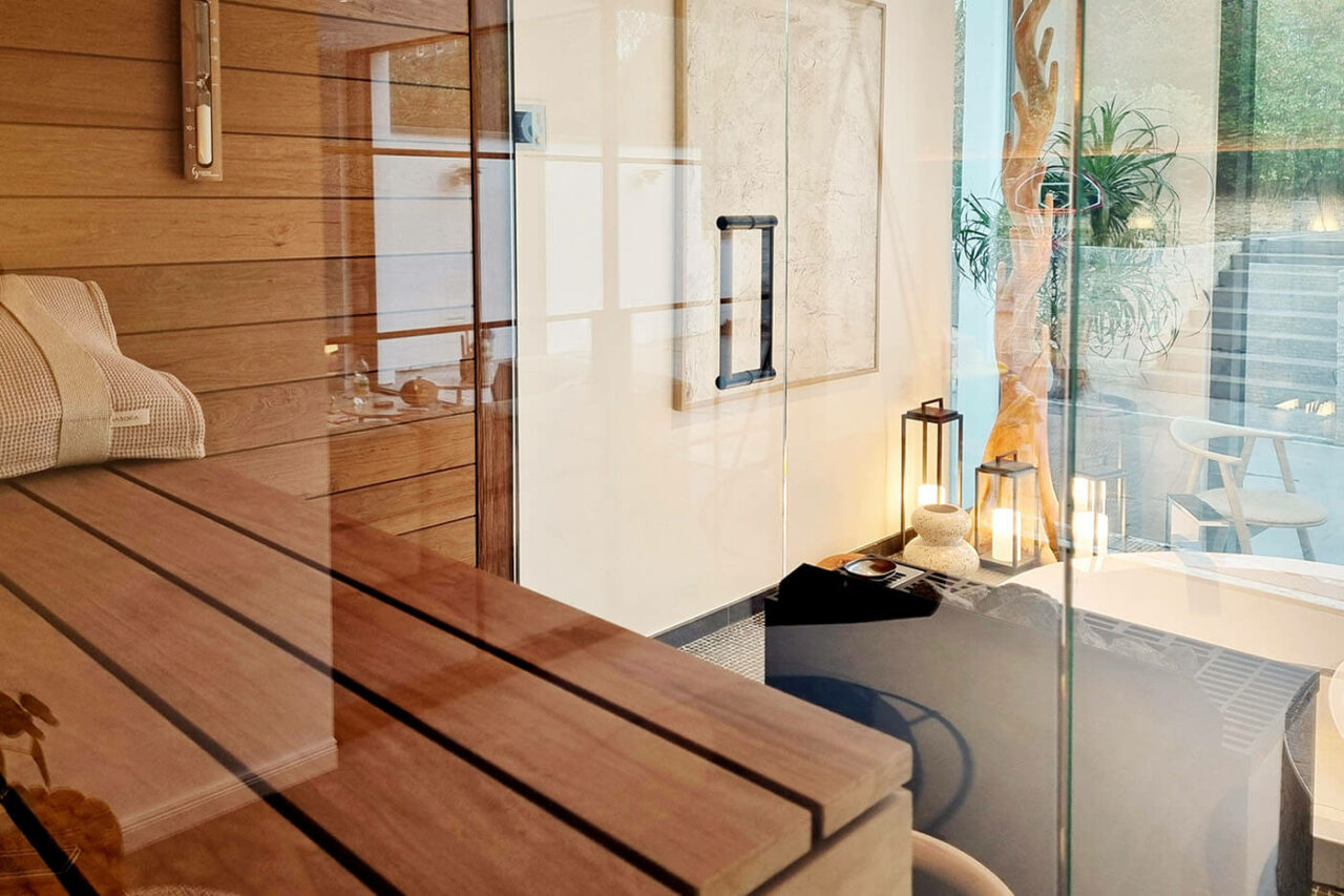 Design Ecksauna in Thermo Espenholz mit zweiseitige Verglasung und schwebenden Saunabänken. Modernes Bad in schwarz-weißer Gestaltung mit eingelassener Badewanne. Sauna nach Maß aus der corso sauna manufaktur.