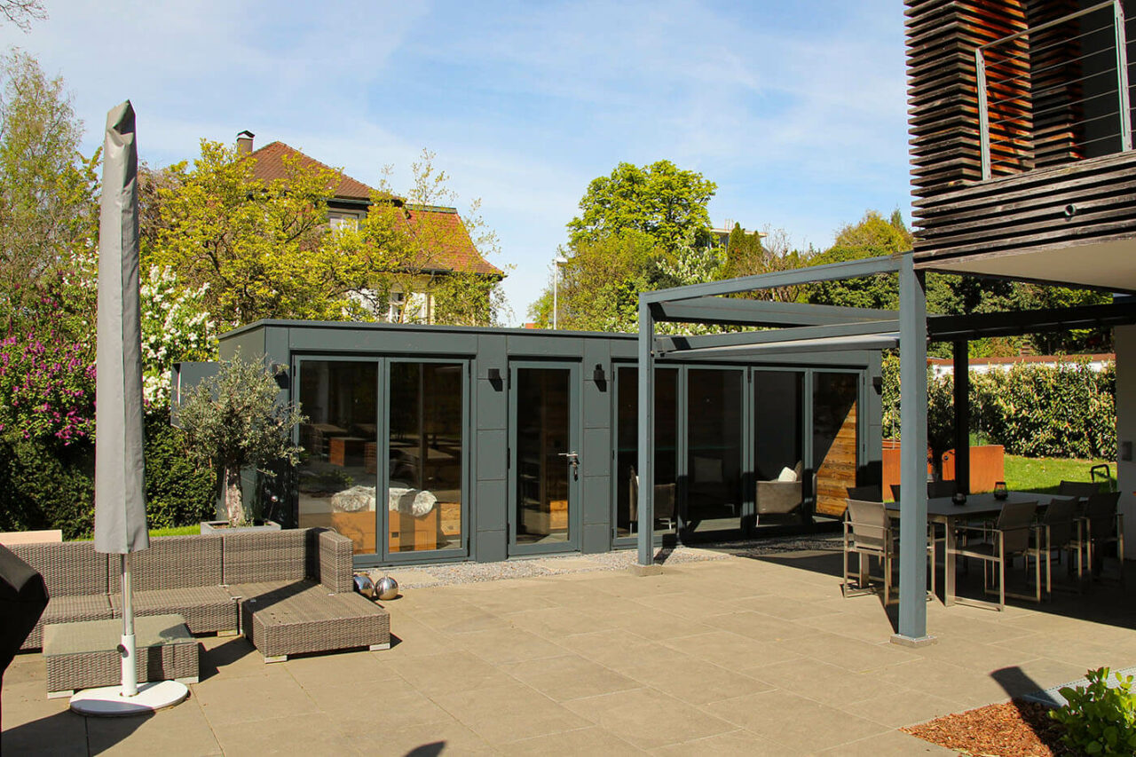 Poolhaus nach Maß mit zu öffnender Glasfront, Daybed, Kaffeeküche und Lounge. Außenverkleidung in wetterfesten Trespa Schichtstoffplatten.