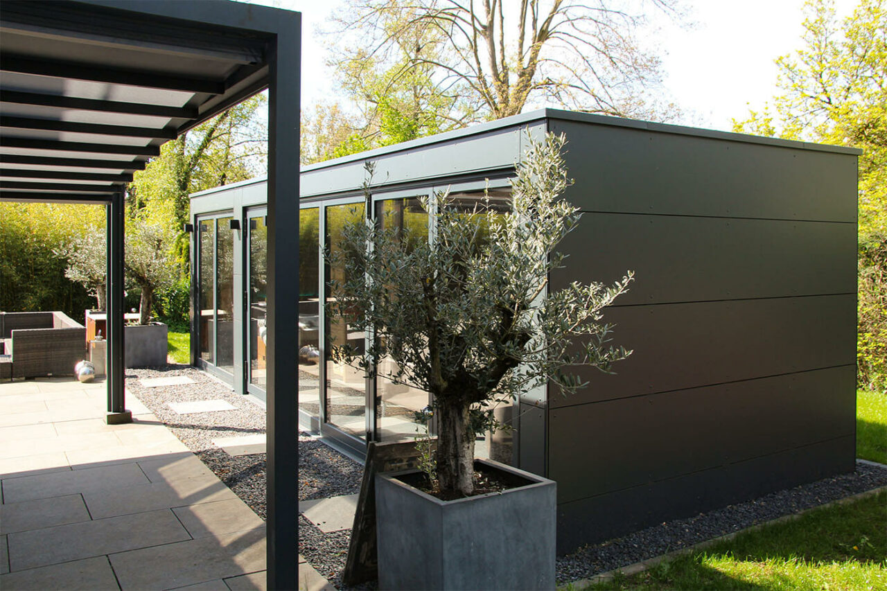 Poolhaus nach Maß mit zu öffnender Glasfront, Daybed, Kaffeeküche und Lounge. Außenverkleidung in wetterfesten Trespa Schichtstoffplatten.