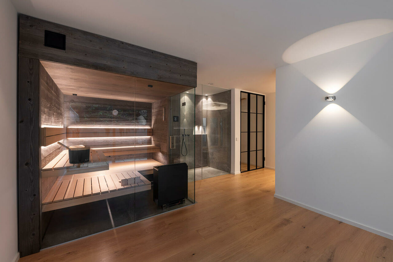 Sauna nach Maß: Sauna in grauem Altholz mit großzügiger Verglasung, schwebenden Saunabänken vor der Glasfront und indirekter LED Beleuchtung. Maßanfertigung.
