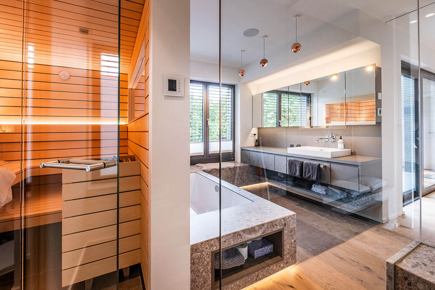 Sauna im Bad in heller Espe mit Glastür und Indoor-Fenster Richtung Bad. Designsauna nach Maß mit Doppelnutprofil und indirekter LED Beleuchtung.